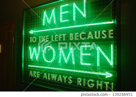A bright green neon sign displays gender-specific bathroom instructions with a joke 139286951