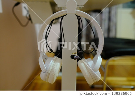 A pair of white headphones hangs on a white table stand A pair of white headphones hangs on a white table stand 139286965