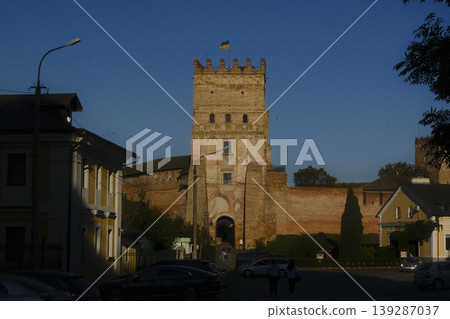 Lubart's castle tower with Ukrainian flag overlooks cars and nearby buildings in Lutsk Lubart's castle tower with Ukrainian flag overlooks cars and nearby buildings in Lutsk 139287037