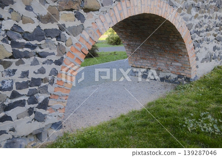 A stone arch with bricks forms a passage. The archway leads to a park path 139287046