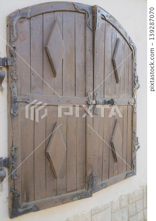 Rustic wooden shutters with metal hardware remain secured to the side of a building Rustic wooden shutters with metal hardware remain secured to the side of a building 139287070