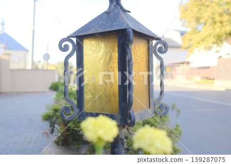 Decorative streetlight sits on a sidewalk with yellow flowers in a town setting 139287075