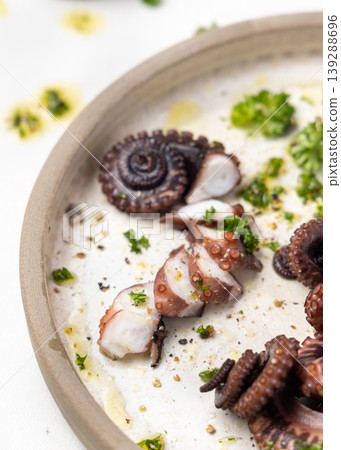 Boiled octopus tentacles and sliced pieces on ceramic plate top view. Olive oil and parsley dressing Boiled octopus tentacles and sliced pieces on ceramic plate top view. Olive oil and parsley dressing 139288696