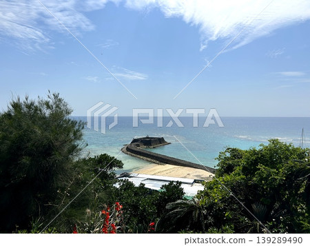 A breakwater and the blue sea of Okinawa, seen through tropical plants and red flowers. A breakwater and the blue sea of Okinawa, seen through tropical plants and red flowers. 139289490