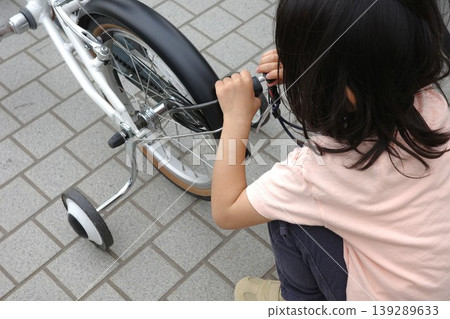 A child in a short-sleeved shirt practicing how to unlock a bicycle. 139289633