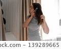 A woman combs her hair in front of a mirror. She's tidying herself up. She's wearing a casual gray T-shirt. Her expression is focused, as she prepares for the workday. Self-care. Space for text. 139289665