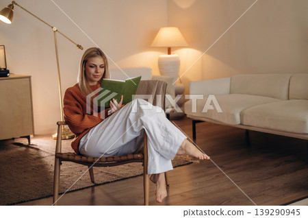 Cozy place, relaxing. A woman is sitting on the chair in the room and reading the book 139290945