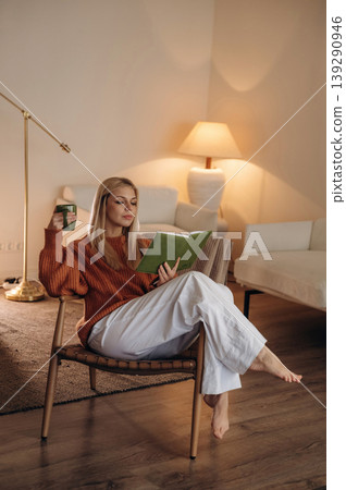 Cozy place, relaxing. A woman is sitting on the chair in the room and reading the book Cozy place, relaxing. A woman is sitting on the chair in the room and reading the book 139290946
