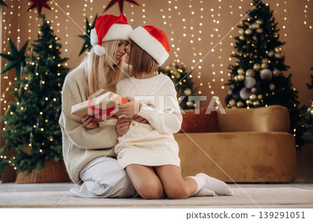 Gift in the box, holding it. Mother and daughter are celebrating New Year at home in domestic room Gift in the box, holding it. Mother and daughter are celebrating New Year at home in domestic room 139291051