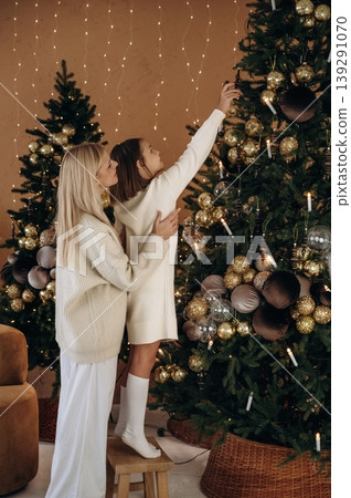 Helping to decorate the tree. Mother and daughter are celebrating New Year at home in domestic room Helping to decorate the tree. Mother and daughter are celebrating New Year at home in domestic room 139291070
