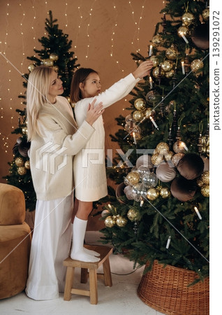 Helping to decorate the tree. Mother and daughter are celebrating New Year at home in domestic room Helping to decorate the tree. Mother and daughter are celebrating New Year at home in domestic room 139291072
