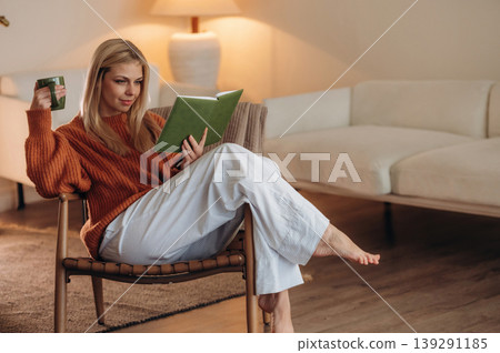 Story time, interesting information. A woman is sitting on the chair in the room and reading the book Story time, interesting information. A woman is sitting on the chair in the room and reading the book 139291185