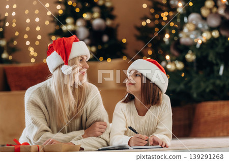Process of writing the letter to Santa. Mother and daughter are celebrating New Year at home in domestic room Process of writing the letter to Santa. Mother and daughter are celebrating New Year at home in domestic room 139291268