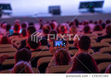Audience recording presentation with smartphone at conference in dim auditorium full of attendees Audience recording presentation with smartphone at conference in dim auditorium full of attendees 139291360