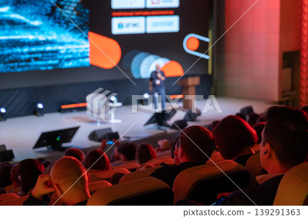 Audience watching speaker on stage during business and technology conference presentation with large LED screen 139291363