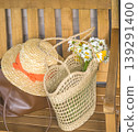 Bouquet of white daisy flowers in a wicker bag, straw hat on a wooden bench 139291400