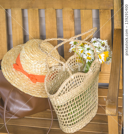 Bouquet of white daisy flowers in a wicker bag, straw hat on a wooden bench Bouquet of white daisy flowers in a wicker bag, straw hat on a wooden bench 139291400