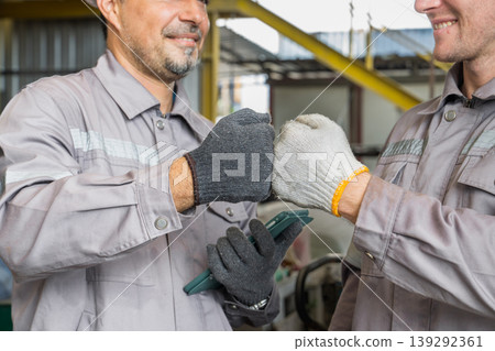 Caucasian and Middle Eastern mid-adult male mechanics fist bumping by truck in Asian industrial yard Caucasian and Middle Eastern mid-adult male mechanics fist bumping by truck in Asian industrial yard 139292361