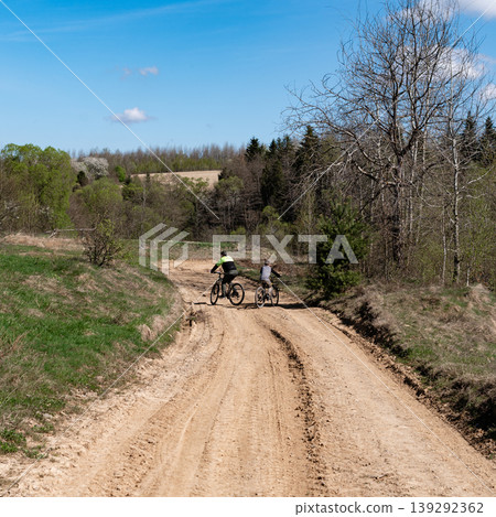 Two cyclists enjoying a scenic bike ride on a dirt road, surrounded by trees and fields. Two cyclists enjoying a scenic bike ride on a dirt road, surrounded by trees and fields. 139292362