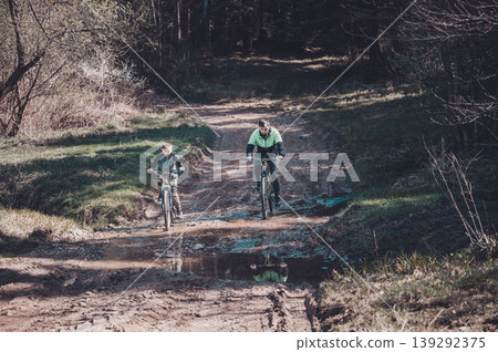 Father and son enjoy a bike ride on a muddy trail through the woods. Father and son enjoy a bike ride on a muddy trail through the woods. 139292375