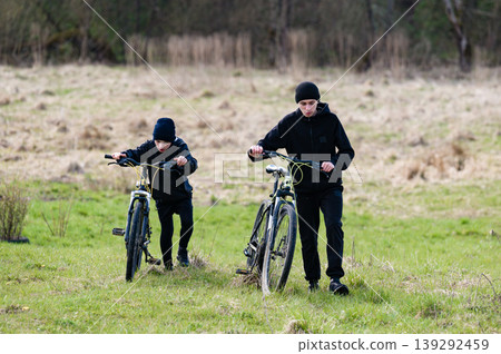 Two boys walk their bikes across a grassy field, enjoying an outdoor adventure. 139292459