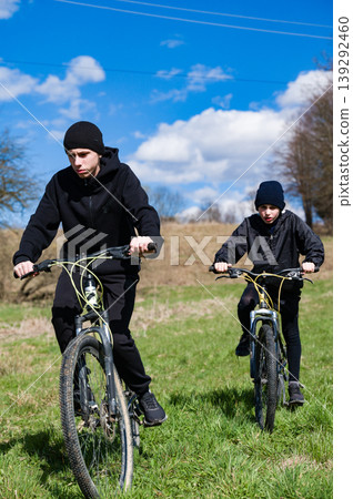 Two young cyclists enjoying a sunny day outdoors, riding their bikes across a grassy field. Two young cyclists enjoying a sunny day outdoors, riding their bikes across a grassy field. 139292460