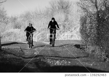 Two boys cycling down a country lane on a sunny day. Enjoyable outdoor activity. 139292463