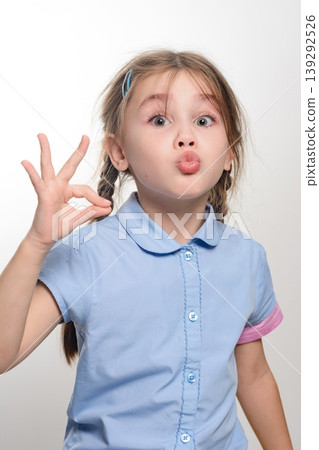Cute girl showing okay sign with a funny face. Playful expression, positive gesture. Cute girl showing okay sign with a funny face. Playful expression, positive gesture. 139292526