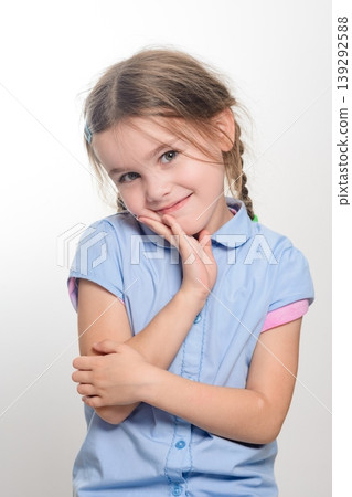 Adorable young girl with pigtails, wearing a light blue shirt, smiles shyly. Adorable young girl with pigtails, wearing a light blue shirt, smiles shyly. 139292588