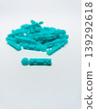 Close up view of a single turquoise blood lancet in focus with a blurred pile of lancets in the background, isolated on a white surface 139292618