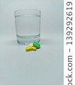 Front view of colorful medicine pills and a clear glass of water on a plain white background. 139292619