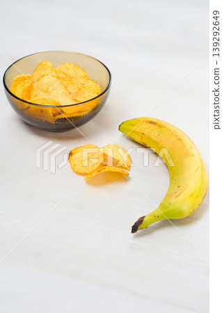 Chips and a banana on a white table. 139292649