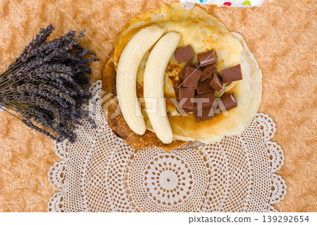 Pancakes with banana and chocolate pieces on a decorative placemat. Pancakes with banana and chocolate pieces on a decorative placemat. 139292654