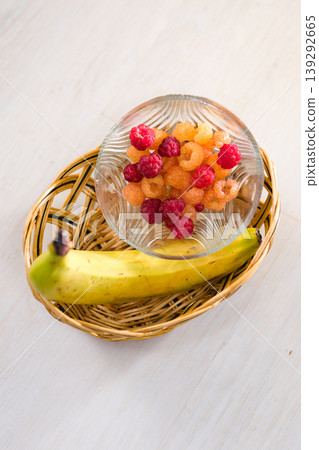 Fresh raspberries and a banana in a basket on a white table. 139292665