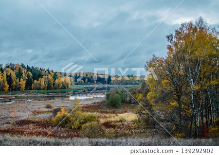 Autumn landscape with colorful trees and calm river under cloudy sky in rural area 139292902