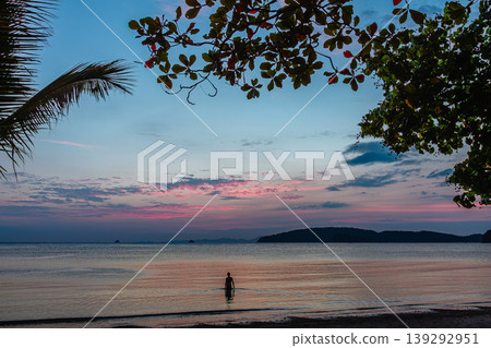Sunset over calm beach with fishing boats and silhouetted trees in the evening sky Sunset over calm beach with fishing boats and silhouetted trees in the evening sky 139292951
