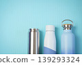 Three reusable drink bottles stainless can, insulated white bottle, and blue travel flask side by side on a textured aqua background, suggesting hydration, eco-friendly lifestyle, and modern design. 139293324