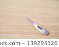 Purple and white digital thermometer lying on a light wooden table, used for measuring body temperature, fever monitoring and home health care. Simple health, illness and personal care concepts. 139293326