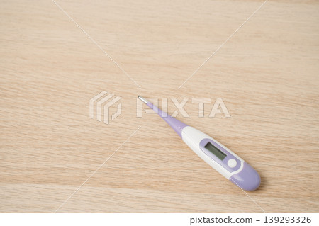 Purple and white digital thermometer lying on a light wooden table, used for measuring body temperature, fever monitoring and home health care. Simple health, illness and personal care concepts. Purple and white digital thermometer lying on a light wooden table, used for measuring body temperature, fever monitoring and home health care. Simple health, illness and personal care concepts. 139293326