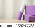 Purple insulated water bottle leaning against two matching yoga blocks on a wooden surface, evoking fitness, hydration, yoga practice and a calming, minimalist wellness studio atmosphere. 139293328