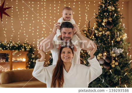 Parents with little baby are celebrating Christmas at home in decorated room Parents with little baby are celebrating Christmas at home in decorated room 139293586