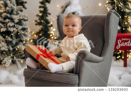 Little baby is sitting indoors in the Christmas decorated room Little baby is sitting indoors in the Christmas decorated room 139293693