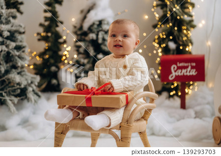 Little baby is sitting indoors in the Christmas decorated room Little baby is sitting indoors in the Christmas decorated room 139293703