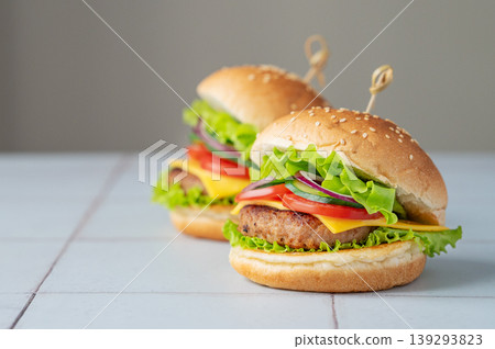Two meat burgers with tomato, cheese, and lettuce on a table close up on a gray background Two meat burgers with tomato, cheese, and lettuce on a table close up on a gray background 139293823