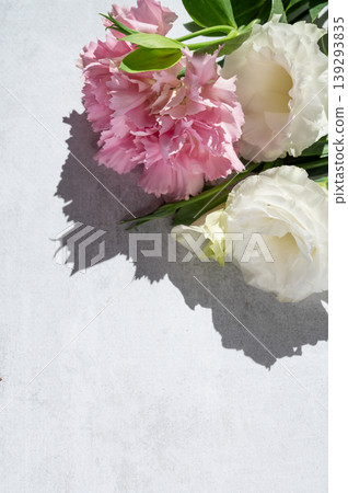 A delicate bouquet of flowers with pink carnations and white eustoma on a light textured background. A delicate bouquet of flowers with pink carnations and white eustoma on a light textured background. 139293835