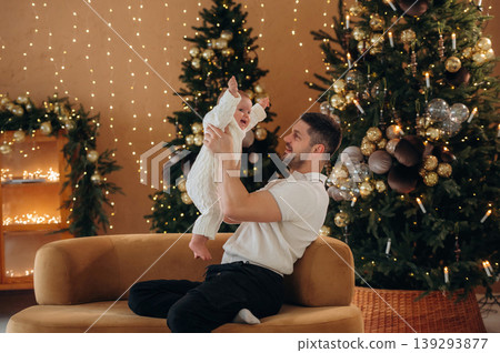 Holding kid in hands. Father with his baby daughter is at home celebrating Christmas Holding kid in hands. Father with his baby daughter is at home celebrating Christmas 139293877