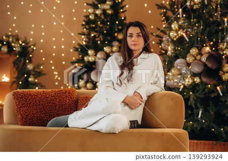 Woman is sitting on the sofa in Christmas decorated room at New Year time celebration Woman is sitting on the sofa in Christmas decorated room at New Year time celebration 139293924