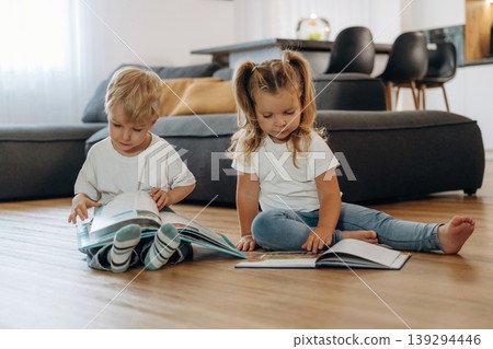 Reading interesting magazine or book. Little kids are playing together in the domestic room at daytime Reading interesting magazine or book. Little kids are playing together in the domestic room at daytime 139294446