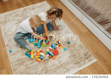 Red, blue, yellow colored objects. Two kids are playing with construction blocks toys at home Red, blue, yellow colored objects. Two kids are playing with construction blocks toys at home 139294468
