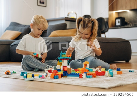 Building the tower, sitting. Two kids are playing with construction blocks toys at home 139294505